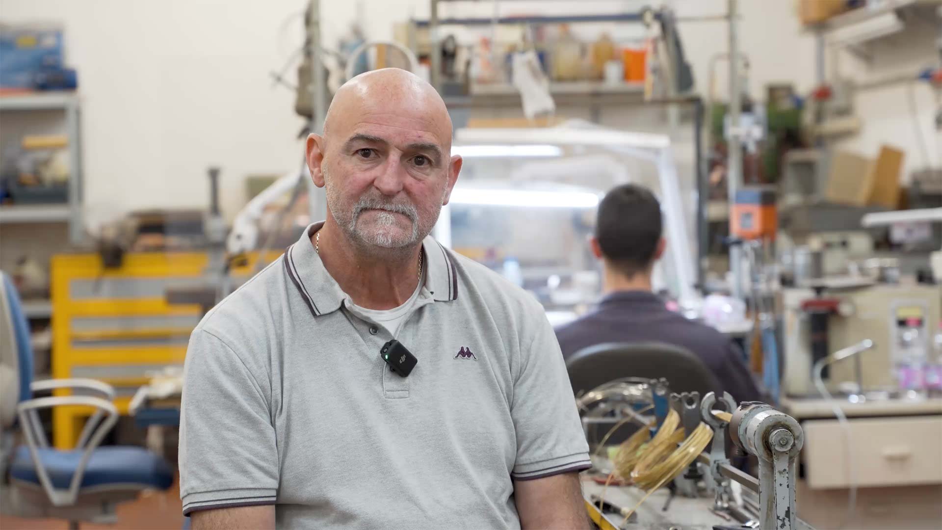 Foto di Marco Fedeli, titolare del laboratorio orafo Queen Gioielli di Verona, con il laboratorio e un operatore sullo sfondo